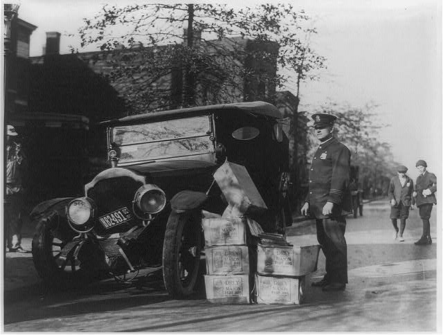 Wikipedia-Rendőr egy összetört autó mellett, amiben több láda „Moonshine”-t, azaz jó minőségű italt találtak (1922)